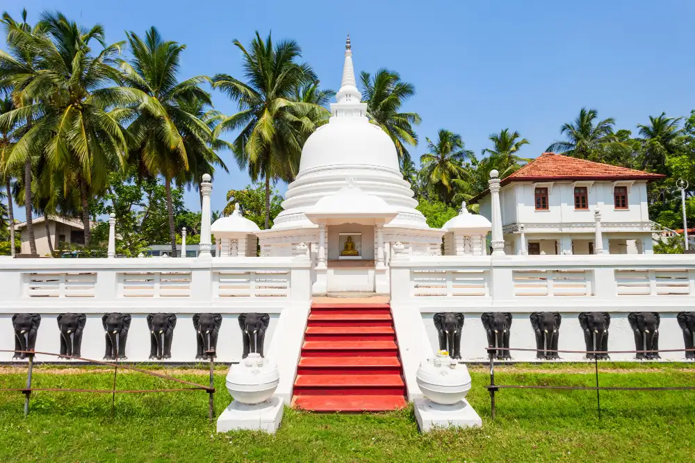 White Buddhist stupa with an elephant-carved boundary wall at a temple in Sri Lanka