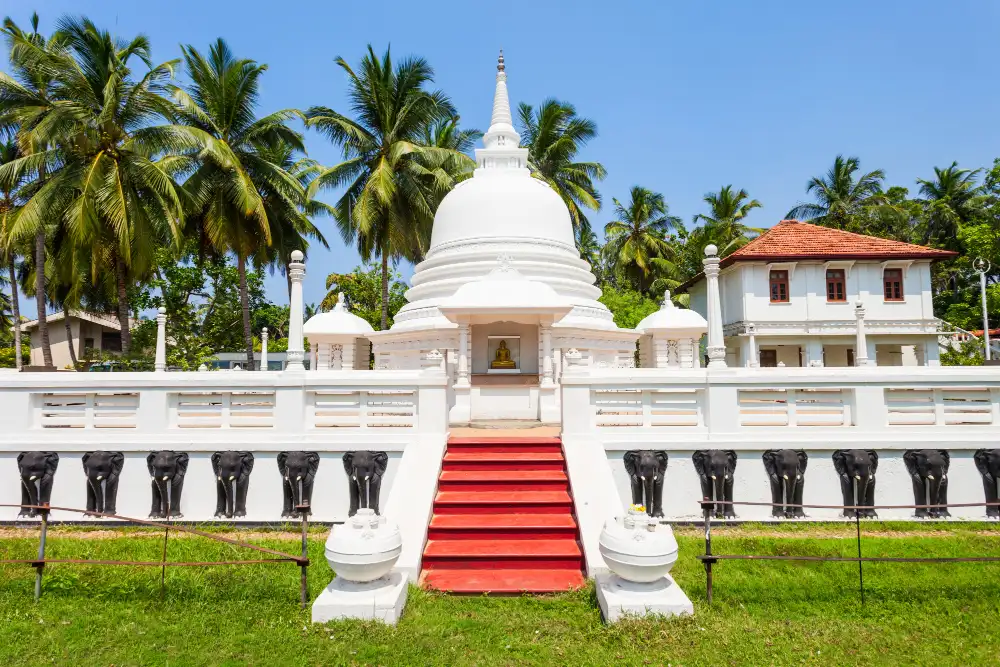 White stupa with red steps and black elephant sculptures along its wall at a Buddhist temple in Sri Lanka